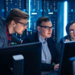 Three masters in cybersecurity students working together at a bay of monitors