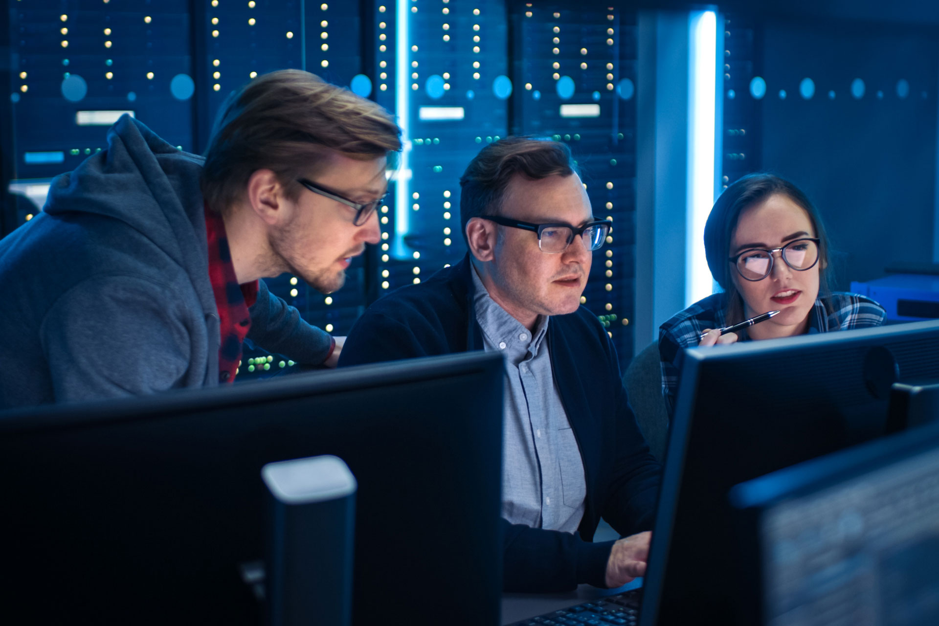 Three masters in cybersecurity students working together at a bay of monitors